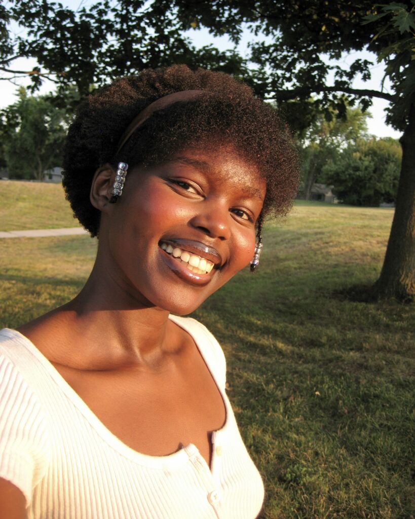 Yar Sudani in natural hair with bangs and a headband. Her makeup is natural and she has on a big smile.