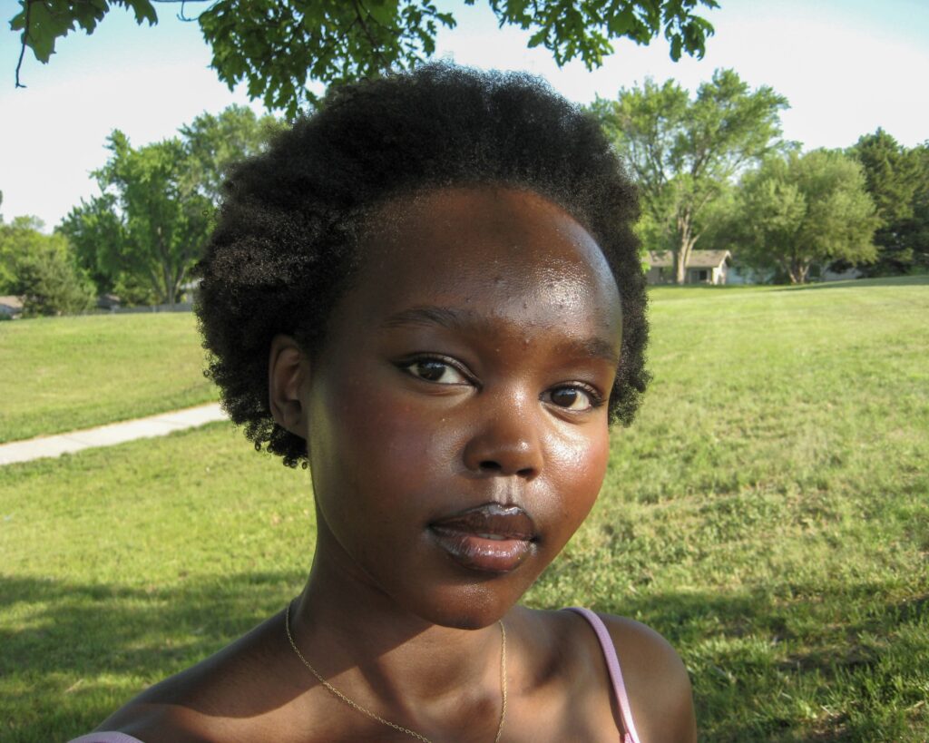 A picture of Yar Sudani with her short natural hair out. She is surrounded by a beautiful green outside setting.