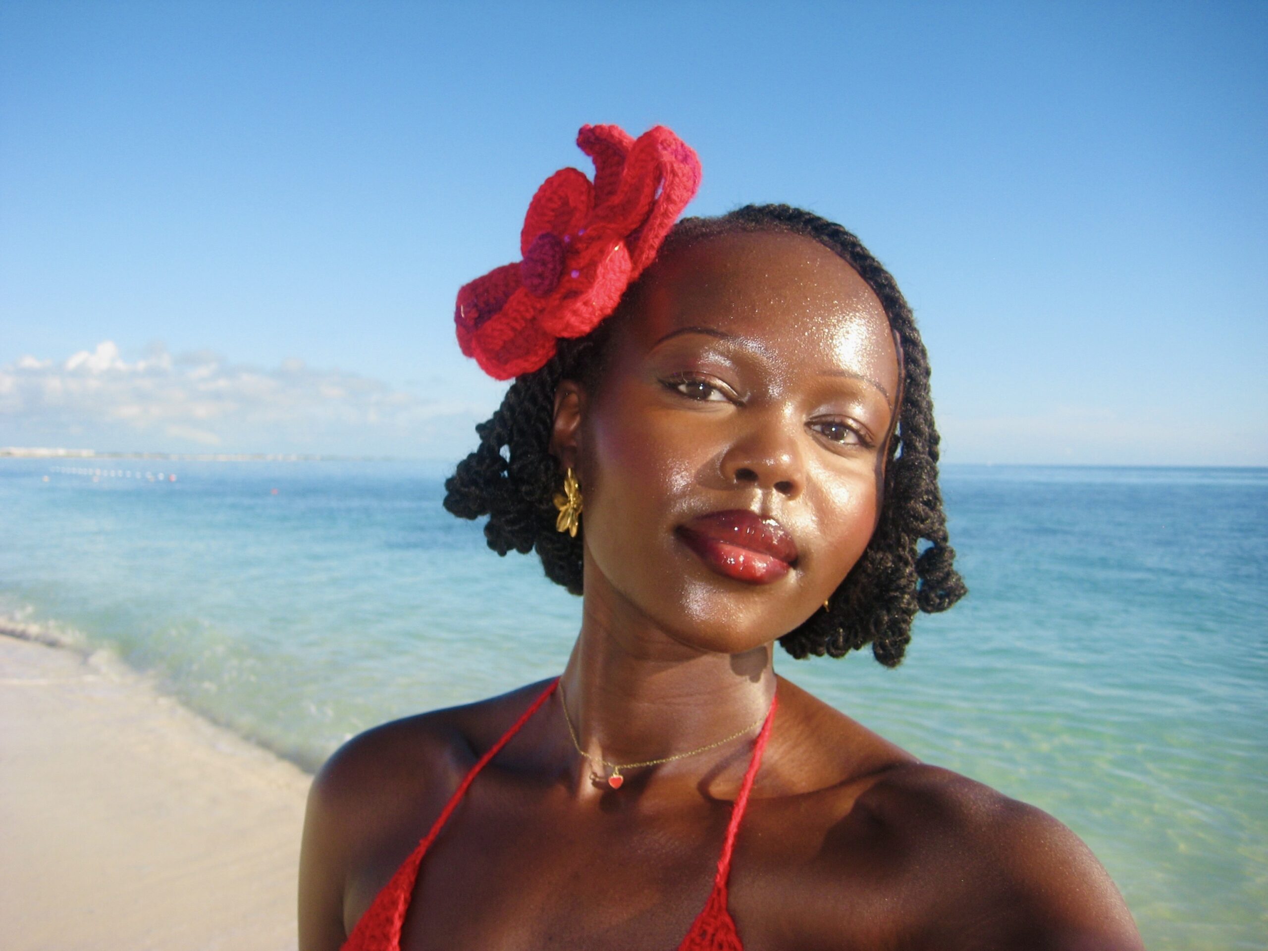 Authur, Yar Sudani, smiling with the backdrop of the sea behind her, and a crochet flower in her hair.